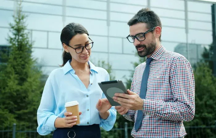 Two professionals outside an office reviewing a tablet, discussing service listings and checks on Local Biz Check